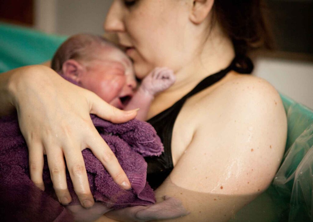 newborn baby is held in a birthing pool after water birth
